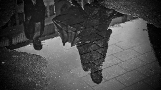 Shadow of people stood in the rain from a puddle