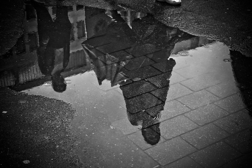 Shadow of people stood in the rain from a puddle