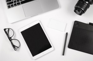A table top with an iPad a laptop, phone, digital camera