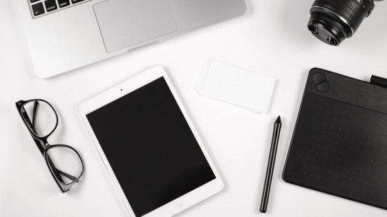 A table top with an iPad a laptop, phone, digital camera