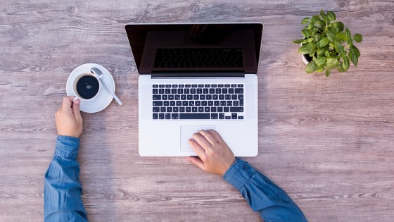 Man on laptop at home drinking coffee at a desk