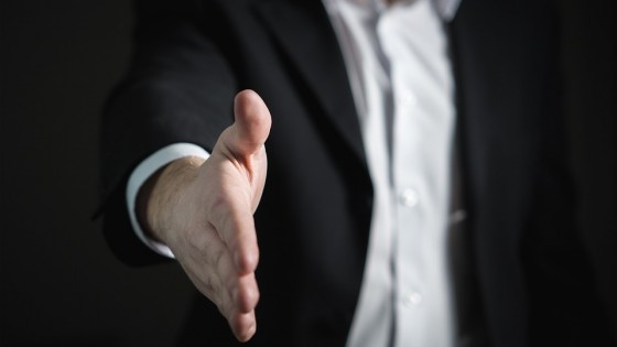 A man in a suit offering his hand out, in a handshake to say 'you got the job'