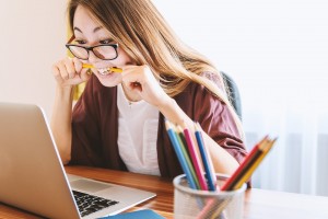 Woman on a laptop chewing on a pen looking stressed