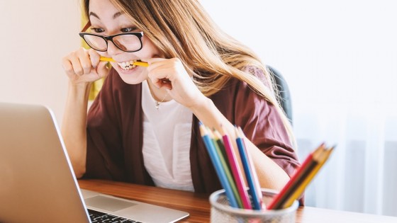 Woman on a laptop chewing on a pen looking stressed
