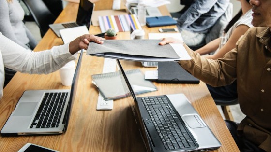 Man and woman arguing over a business file in front of work colleges