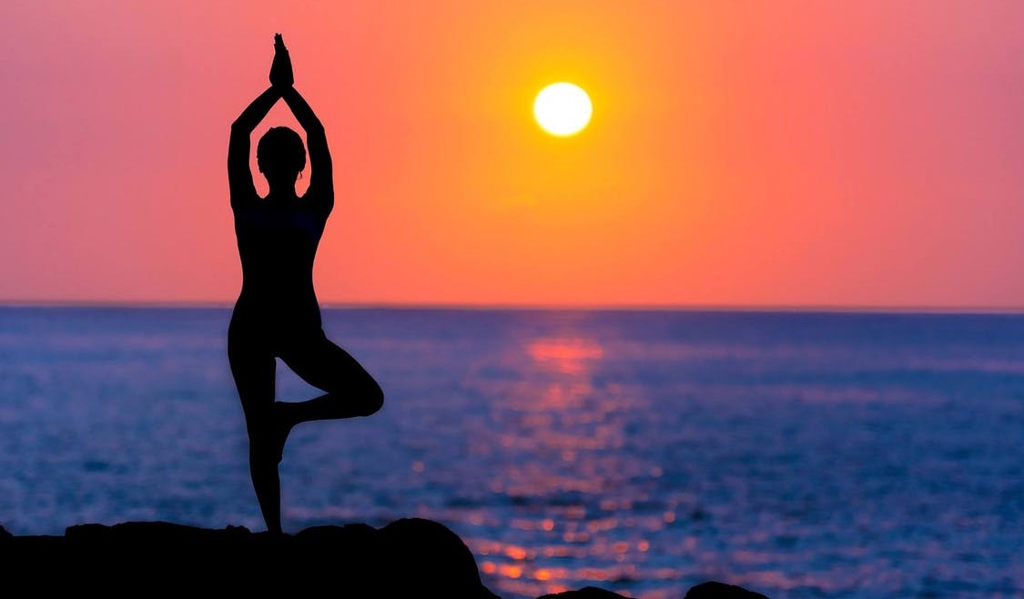 woman doing yoga on a rock by the ocean with a deep red sunset