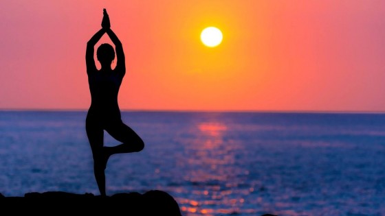 woman doing yoga on a rock by the ocean with a deep red sunset