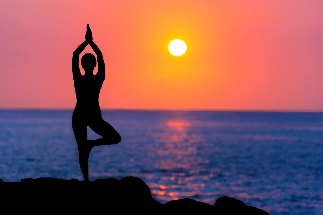 woman doing yoga on a rock by the ocean with a deep red sunset