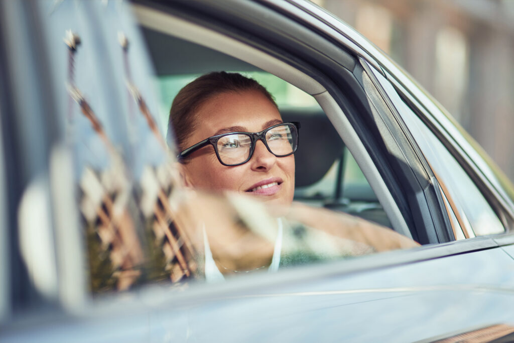 Business trip. Beautiful middle aged business woman wearing eyeglasses looking out of a car window while sitting on back seat in taxi, transportation and vehicle concept